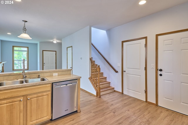 kitchen with light wood-type flooring, stainless steel dishwasher, sink, and hanging light fixtures