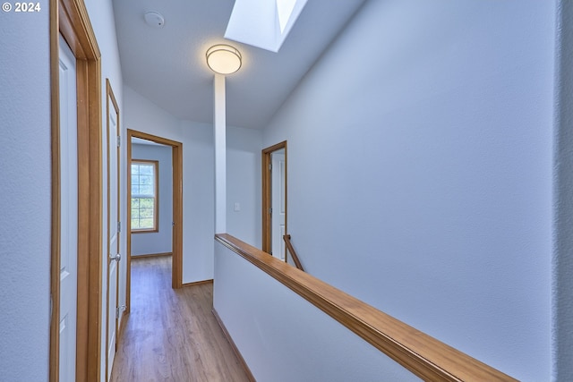 corridor with light wood-type flooring and lofted ceiling with skylight