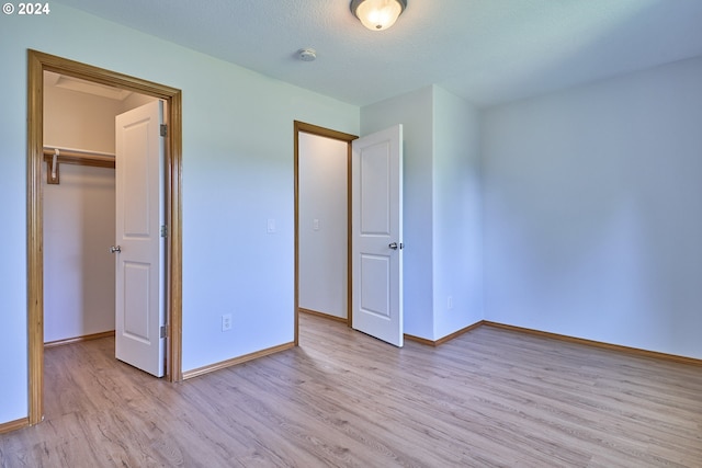 unfurnished bedroom with a textured ceiling, light hardwood / wood-style flooring, a walk in closet, and a closet