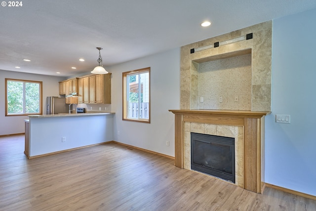 kitchen featuring light hardwood / wood-style flooring, decorative light fixtures, a tile fireplace, kitchen peninsula, and stainless steel fridge with ice dispenser