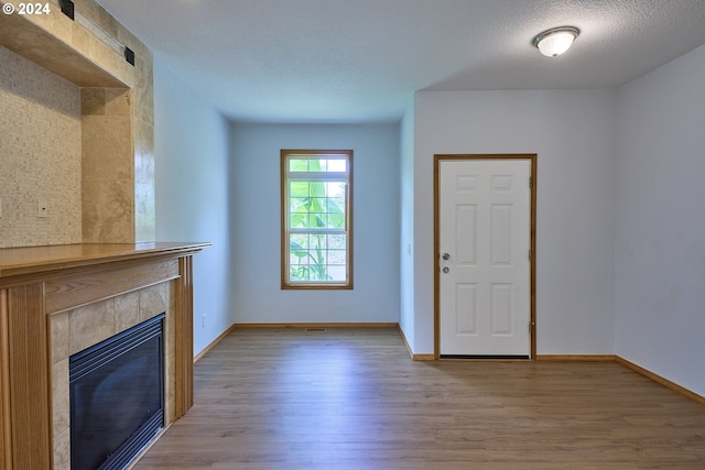 unfurnished living room with a textured ceiling, hardwood / wood-style floors, and a tile fireplace