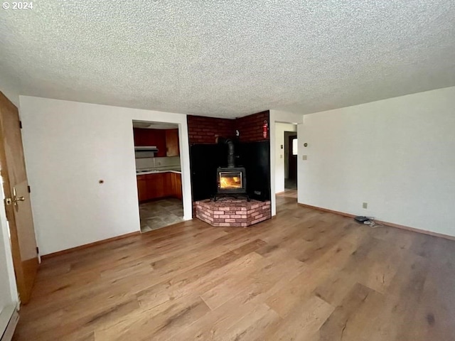 unfurnished living room with a wood stove, light wood-type flooring, and a textured ceiling