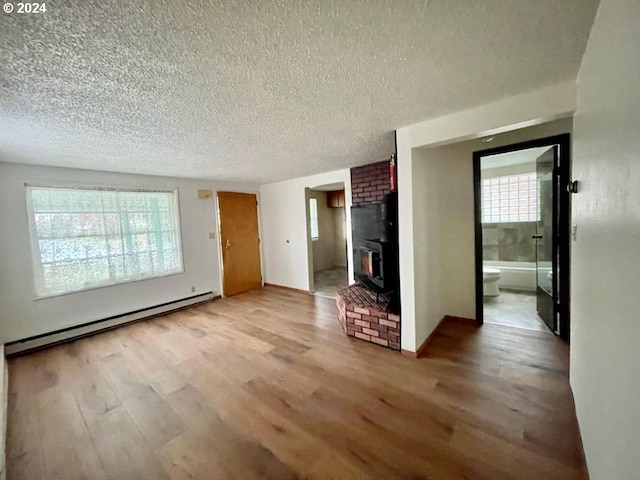 unfurnished living room featuring a baseboard heating unit, a textured ceiling, wood finished floors, and a wood stove