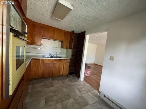 kitchen with hardwood / wood-style floors, a textured ceiling, sink, oven, and baseboard heating