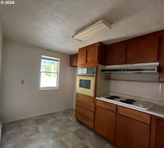 kitchen with wall oven, brown cabinetry, light countertops, under cabinet range hood, and a textured ceiling