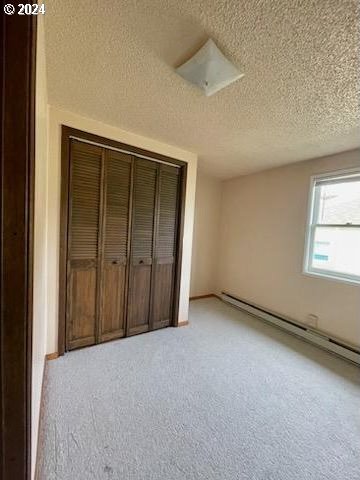 unfurnished bedroom featuring a textured ceiling, a closet, and a baseboard radiator