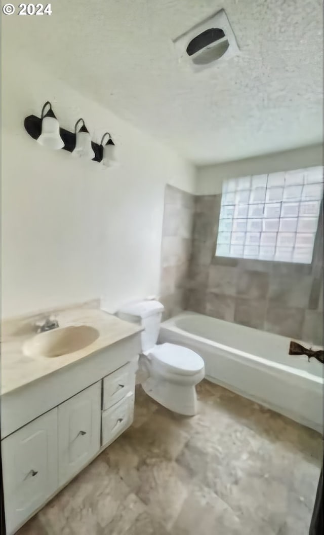 full bathroom with a textured ceiling, vanity, tiled shower / bath combo, and toilet