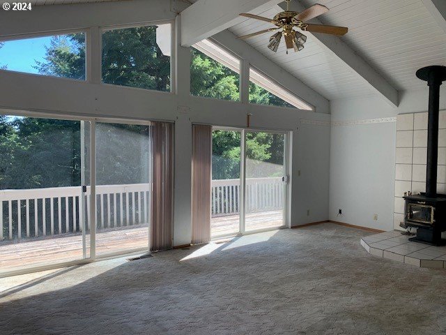 unfurnished living room with a wood stove, ceiling fan, carpet floors, high vaulted ceiling, and beam ceiling