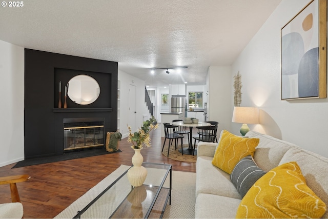 living room featuring dark hardwood / wood-style floors, a large fireplace, a textured ceiling, and track lighting