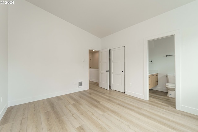 unfurnished bedroom featuring light wood-type flooring, ensuite bathroom, and lofted ceiling