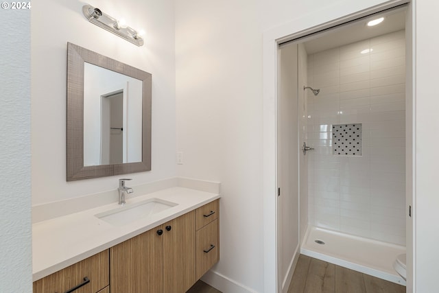 bathroom featuring toilet, hardwood / wood-style floors, vanity, and tiled shower