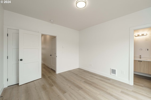 unfurnished bedroom with light wood-type flooring and connected bathroom