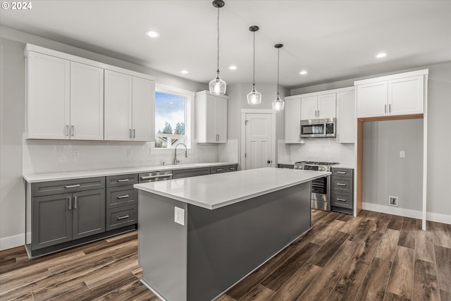 kitchen featuring appliances with stainless steel finishes, sink, a center island, white cabinetry, and hanging light fixtures