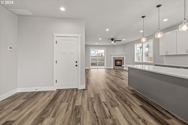 unfurnished living room featuring a stone fireplace, ceiling fan, and dark wood-type flooring