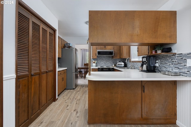 kitchen with decorative backsplash, kitchen peninsula, stainless steel appliances, light hardwood / wood-style flooring, and sink