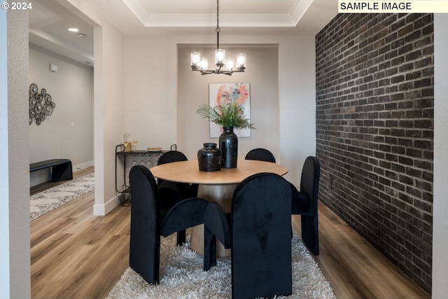 dining space featuring hardwood / wood-style flooring, a notable chandelier, a raised ceiling, and brick wall