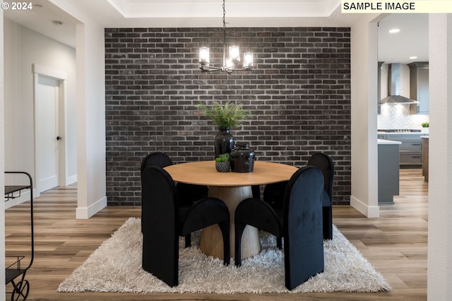 dining area with a chandelier, light wood-type flooring, a raised ceiling, and brick wall