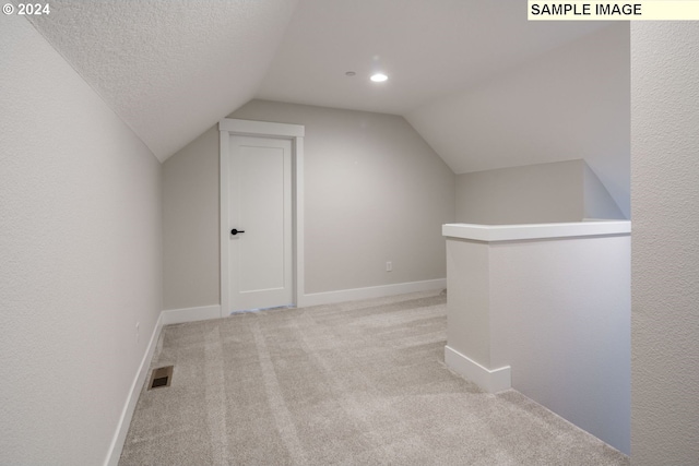 additional living space with a textured ceiling, light colored carpet, and lofted ceiling