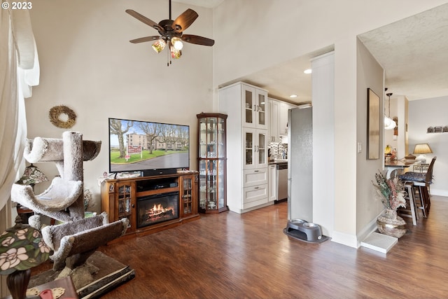 living room with a high ceiling, ceiling fan, decorative columns, and dark hardwood / wood-style flooring