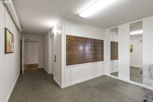 hallway featuring a textured ceiling, a mail area, and dark tile patterned floors