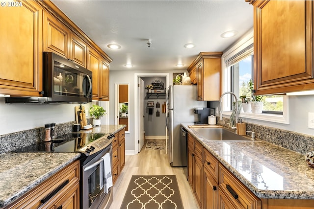 kitchen with light stone countertops, stainless steel appliances, sink, and light wood-type flooring