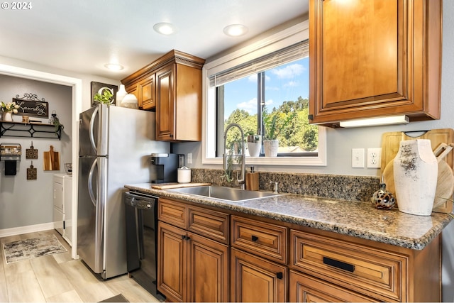 kitchen featuring separate washer and dryer, light wood-type flooring, dark stone counters, dishwasher, and sink