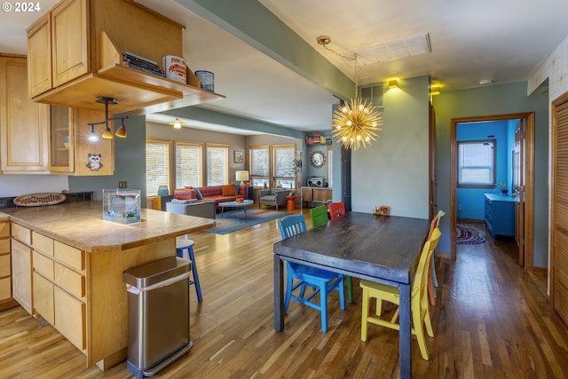 kitchen featuring light brown cabinets, kitchen peninsula, an inviting chandelier, light hardwood / wood-style flooring, and decorative light fixtures