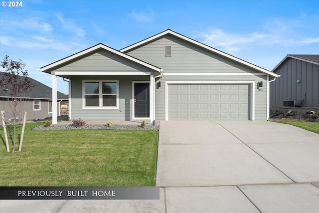 view of front facade featuring a front yard, central AC unit, and a garage