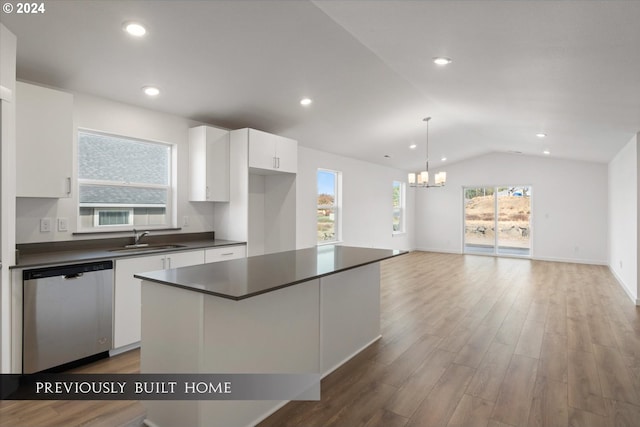 kitchen with dark countertops, stainless steel dishwasher, white cabinets, vaulted ceiling, and a sink