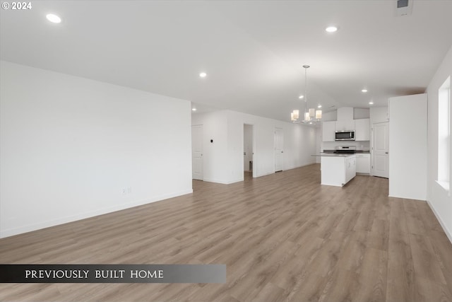 unfurnished living room featuring light wood-style floors, vaulted ceiling, a notable chandelier, and recessed lighting