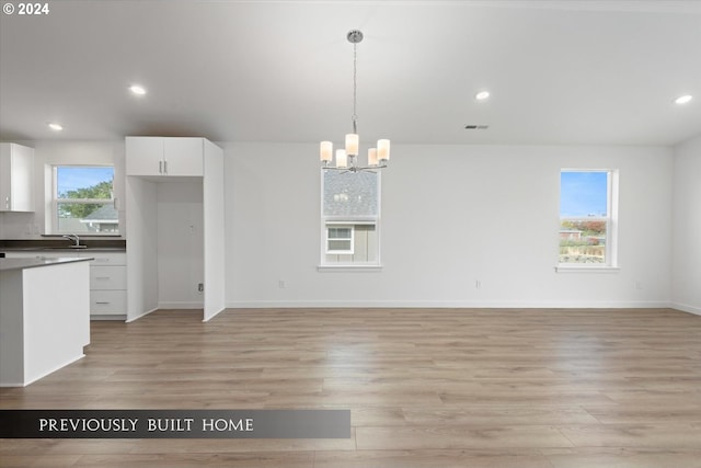 interior space with visible vents, dark countertops, light wood-style flooring, decorative light fixtures, and white cabinetry