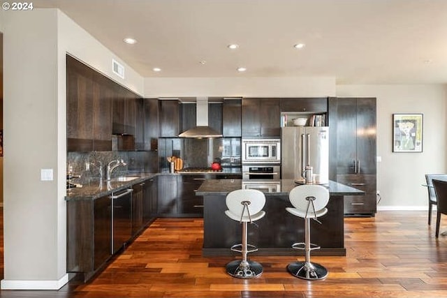 kitchen featuring wall chimney range hood, tasteful backsplash, a breakfast bar, a kitchen island, and appliances with stainless steel finishes