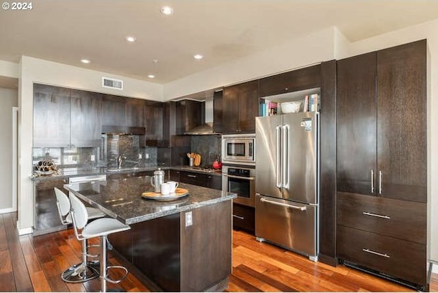 kitchen featuring decorative backsplash, appliances with stainless steel finishes, dark hardwood / wood-style flooring, dark stone countertops, and a center island