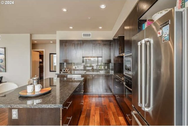 kitchen with decorative backsplash, dark stone counters, stainless steel appliances, dark hardwood / wood-style floors, and a kitchen island