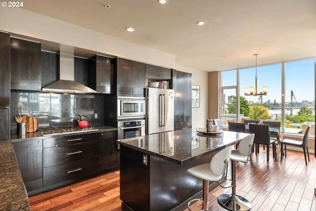 kitchen with a kitchen breakfast bar, wall chimney exhaust hood, decorative light fixtures, light hardwood / wood-style floors, and stainless steel appliances