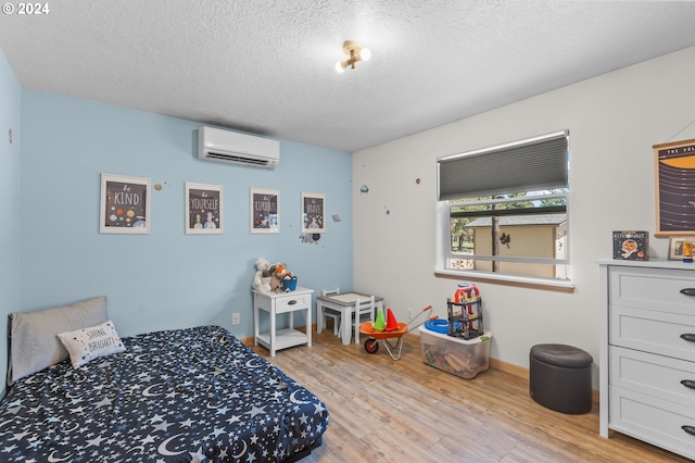 bedroom with an AC wall unit, a textured ceiling, and light wood-type flooring