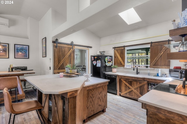 kitchen featuring sink, a barn door, light hardwood / wood-style floors, a kitchen island, and black appliances