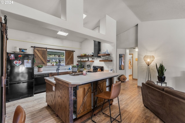 kitchen with black appliances, light hardwood / wood-style flooring, a barn door, a kitchen island, and a kitchen bar