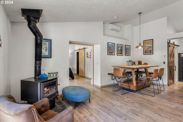 living room featuring light wood-type flooring, a wall mounted AC, a barn door, high vaulted ceiling, and a wood stove