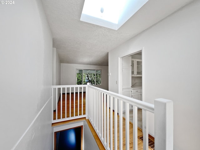 hall featuring hardwood / wood-style floors, a textured ceiling, and a skylight