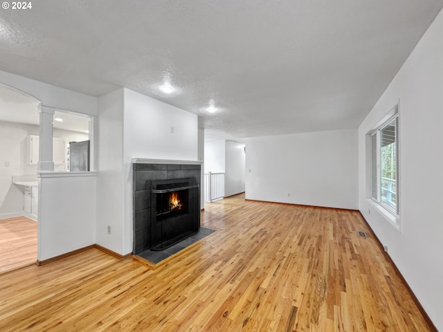 unfurnished living room with a textured ceiling, light hardwood / wood-style flooring, ornate columns, and a tiled fireplace