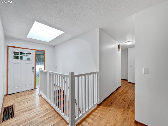 corridor featuring a textured ceiling, light wood-type flooring, and a skylight