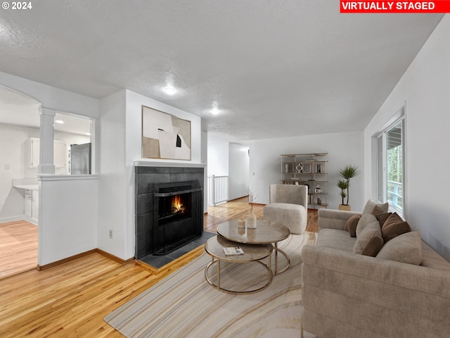 living room featuring ornate columns, hardwood / wood-style floors, a textured ceiling, and a fireplace