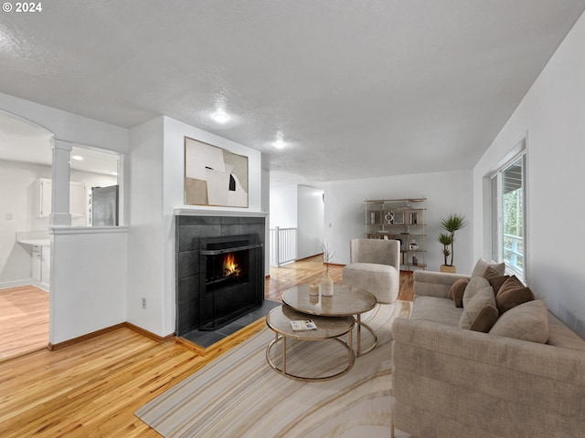 living room featuring a textured ceiling, hardwood / wood-style flooring, a fireplace, and decorative columns