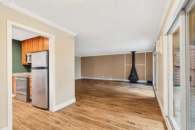 interior space with a wood stove, light wood-type flooring, a baseboard heating unit, and ornamental molding