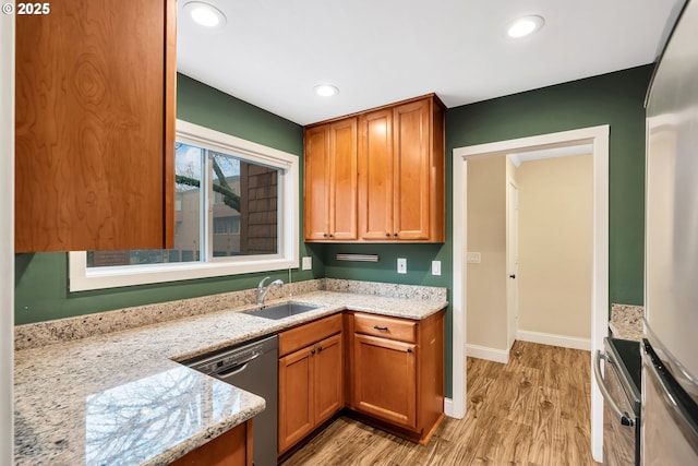 kitchen featuring dishwasher, sink, light wood-type flooring, wall oven, and light stone counters