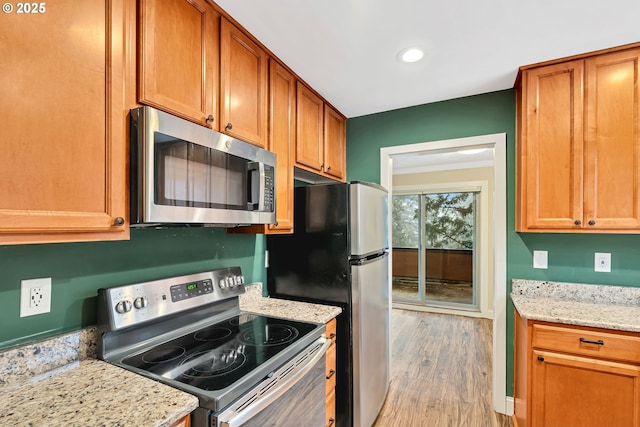 kitchen featuring stainless steel appliances, light stone counters, crown molding, and light hardwood / wood-style flooring