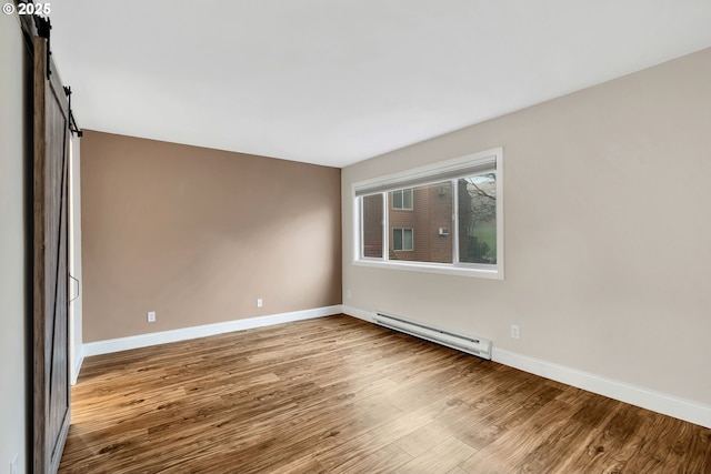 unfurnished room featuring a barn door, light hardwood / wood-style floors, and a baseboard heating unit