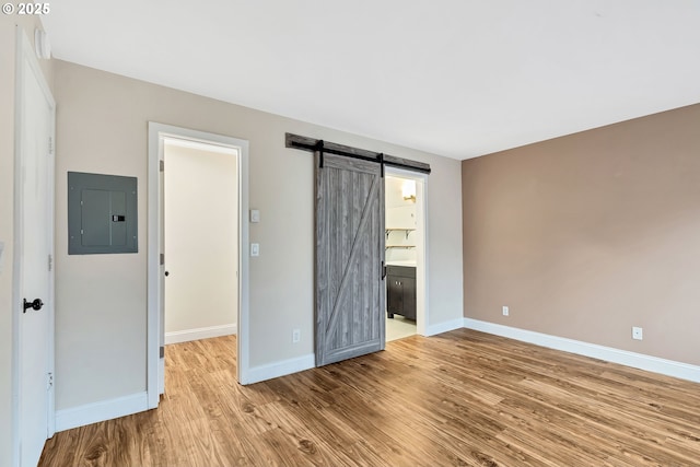 unfurnished bedroom featuring electric panel, ensuite bathroom, a barn door, a spacious closet, and light hardwood / wood-style floors