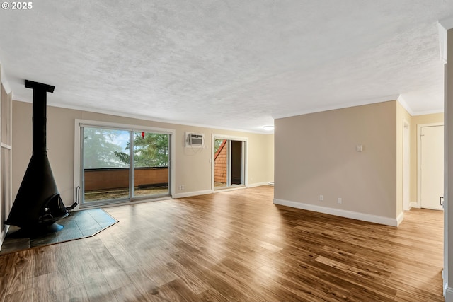 unfurnished living room with a wall unit AC, a wood stove, crown molding, and light wood-type flooring